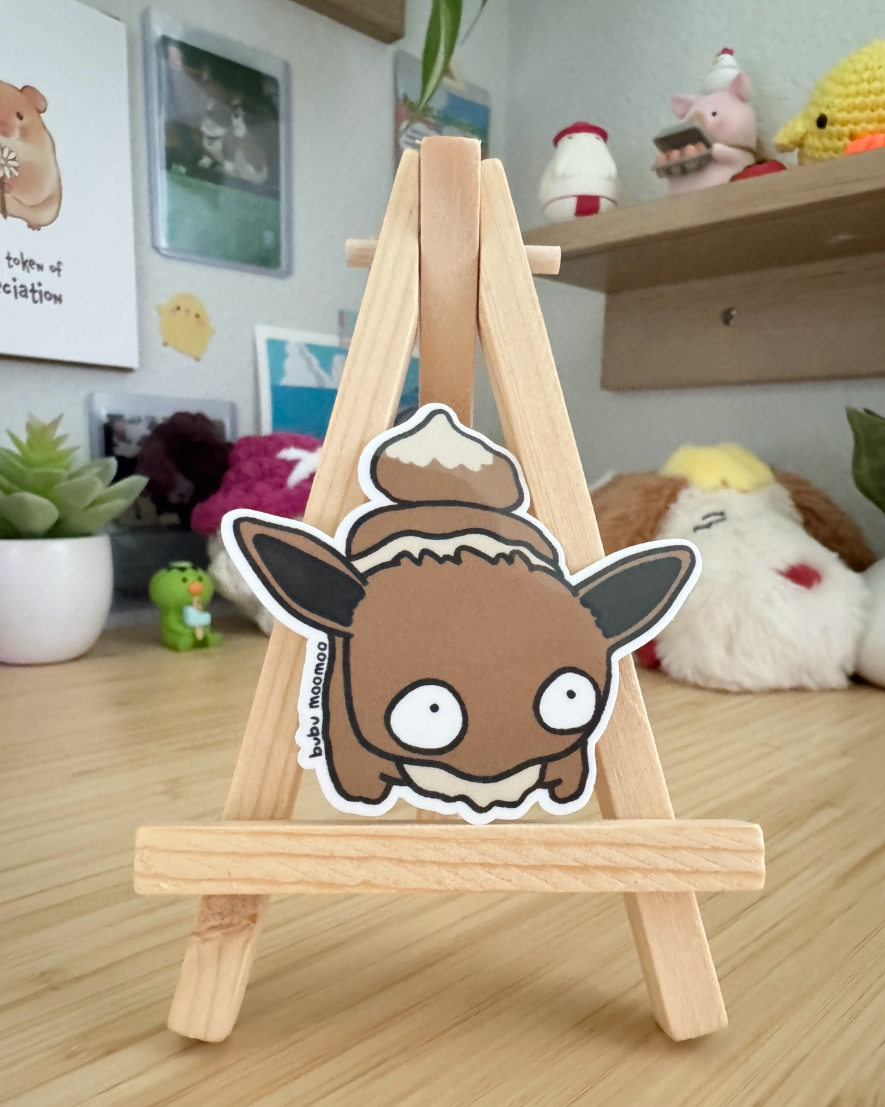 Small wooden easel with a cartoon character sticker of eewee on a wooden desk.