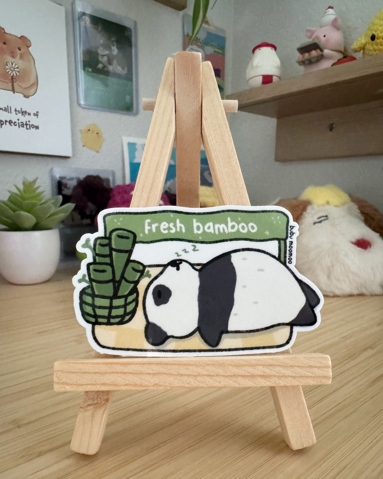 Small wooden easel with a cartoon character sticker of a panda with the words "fresh bamboo" on a wooden desk.