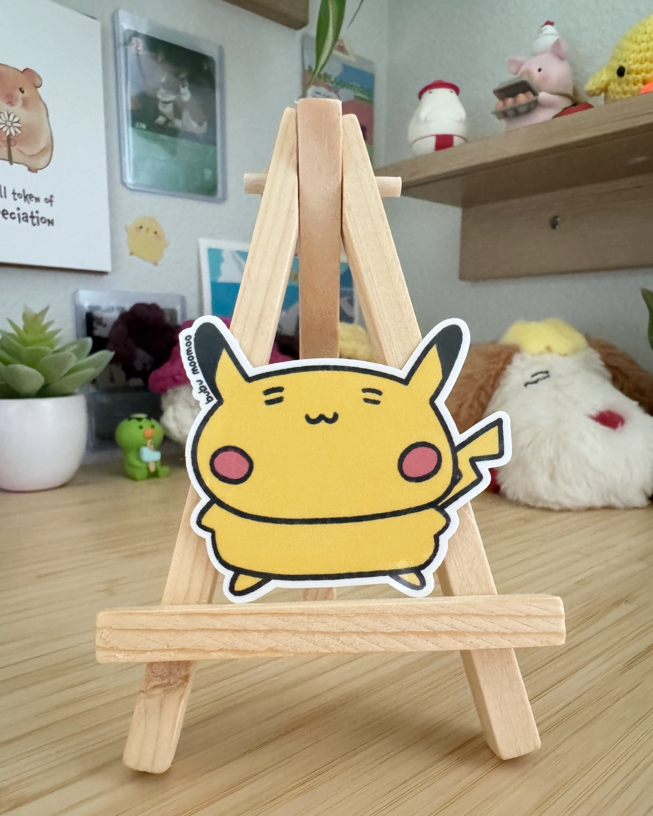 Small wooden easel with a cartoon character sticker of pokacho on a wooden desk.